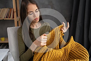 Beautiful girl knits a warm sweater on armchair. Knitting as a hobby. Accessories for knitting.