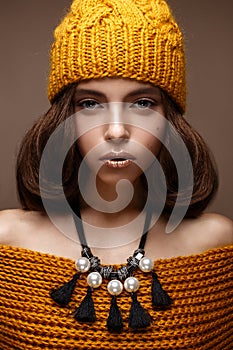 Beautiful girl in a knitted hat on her head and a necklace of pearls around her neck. The model with gentle make-up and gold lips