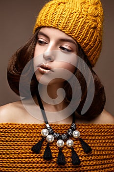 Beautiful girl in a knitted hat on her head and a necklace of pearls around her neck. The model with gentle make-up and gold lips