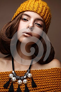 Beautiful girl in a knitted hat on her head and a necklace of pearls around her neck. The model with gentle make-up and gold lips