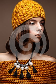 Beautiful girl in a knitted hat on her head and a necklace of pearls around her neck. The model with gentle make-up and gold lips