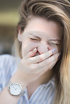 A beautiful girl laughs closing her eyes and covering her mouth with her hand