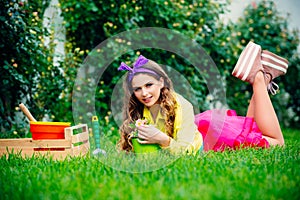 Beautiful girl lie on grass at her spring garden. Young pretty woman enjoy spring nature and take care about her plants
