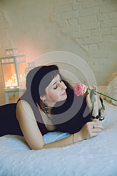 Beautiful girl lies on the bed and holds a rose in her hands