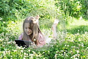 A beautiful girl lies on her stomach and reads a book in the park. Front view