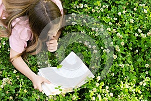 A beautiful girl lies on her stomach and reads a book in the park. View from above