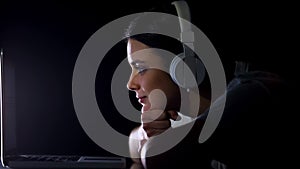 Beautiful girl listening to music in headphones reading social network on laptop