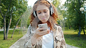 Beautiful girl listening to music in headphones using smartphone in green park