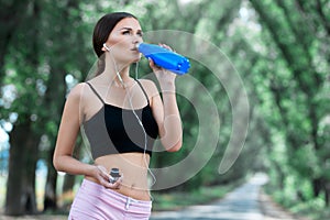 Beautiful girl listens to music on headphones and drinks water after jogging.