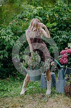 Beautiful girl with long blonde hair holds a watering can with flowers in a blooming garden