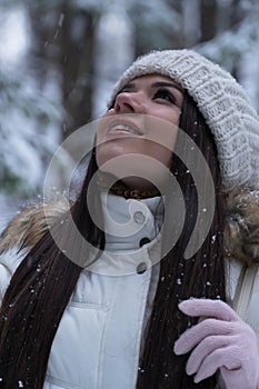 Beautiful girl with long dark hair in a white jacket walking in a winter forest during a snowfall