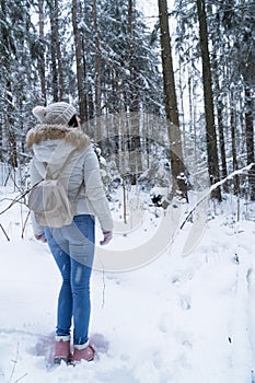 Beautiful girl with long dark hair in a white jacket walking in a winter forest during a snowfall