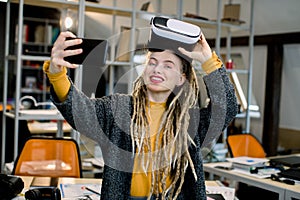 Beautiful girl with long dreadlocks, posing with virtual reality glasses on head, while making selfie photo on her