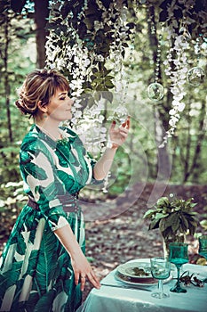 A beautiful girl in a long dress is laying on a table in the woods.