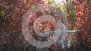 A beautiful girl in a long dress walks in an old abandoned park in the autumn.