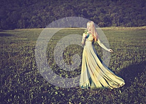 Beautiful girl in long green dress with bouquet of flowers in summer onnature