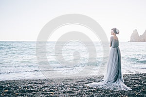 Beautiful girl in a long grey dress with a veil on the beach, waves