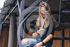 Beautiful girl with long hair and glasses sitting on metal stairs on the wooden background of house with vertical boards. Woman