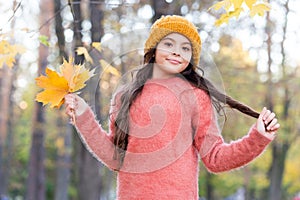 Beautiful girl with long hair hold yellow fallen maple leaves wearing knitted hat and warm sweater in autumn forest
