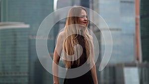 A beautiful girl with long hair is on the roof against the background of the Moscow city business center. She`s wearing