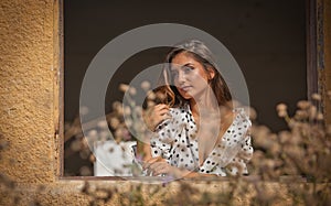 The beautiful and girl with long hair stands by the window.Portrait of a pensive woman looking away through a window.