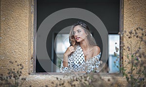 The beautiful and girl with long hair stands by the window.Portrait of a pensive woman looking away through a window.