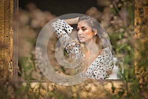 The beautiful and girl with long hair stands by the window.Portrait of a pensive woman looking away through a window.