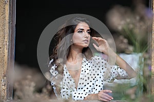 The beautiful and girl with long hair stands by the window.Portrait of a pensive woman looking away through a window.