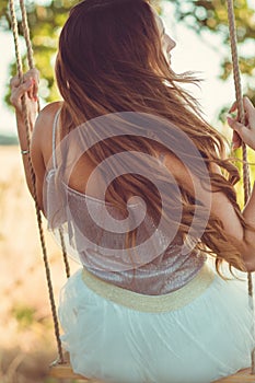 Beautiful girl with long hair swinging on rope swing on summer nature, young woman enjoy flying, leisure activity, lifestyle