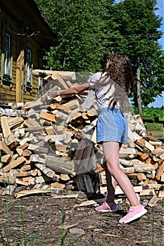 beautiful girl with long hair in white shirt puts firewood in pile. Concept of harvesting firewood for winter.
