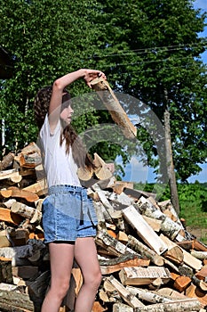 beautiful girl with long hair in white T-shirt and denim shorts puts firewood in pile.