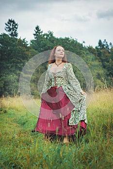 Beautiful girl in long medieval dress walking on summer meadow