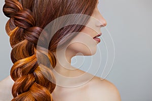 Beautiful girl with long red hair, braided with a French braid, in a beauty salon