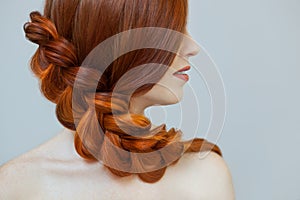 Beautiful girl with long red hair, braided with a French braid, in a beauty salon.