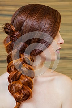 Beautiful girl with long red hair, braided with a French braid, in a beauty salon