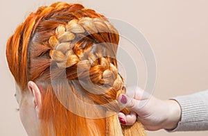 Beautiful girl with long redhair, hairdresser weaves a  braid, close-up in a beauty salon. Professional hair care and creating