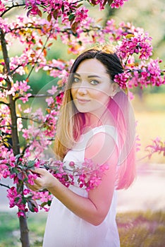 A beautiful girl with long straight hair and big eyes stands in the flowers of a pink Apple tree