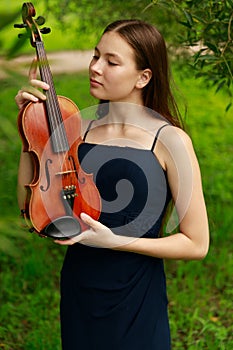 a beautiful girl with long violinists stands in the park in the summer