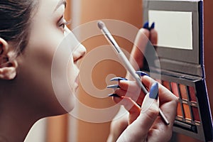 Beautiful girl looking in the mirror doing makeup indoors, young woman applies eye shadow, concept female beauty and cosmetics