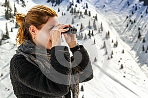 Beautiful girl looks through binoculars on a background of snow-capped mountains