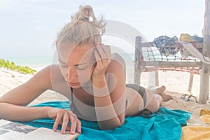 Beautiful girl lying at the beach in her swimsuit and reading a book