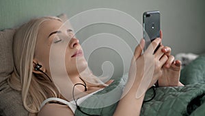 Beautiful girl lying on the bed listening to music with headphones.