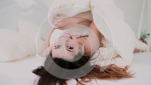 Beautiful girl lying in bed and smiling. Young woman hides under the sheet, flirting with camera.