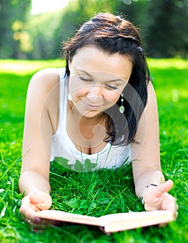 Beautiful girl lying on a grass with book