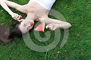 Beautiful girl lying on the grass and eats watermelon