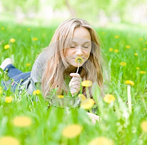 Beautiful girl lying on the grass and smelling dandelion