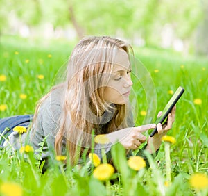 Beautiful girl lying on the grass and using tablet computer