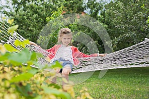Beautiful girl lying on hammock, smiling resting child in spring garden