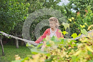 Beautiful girl lying on hammock, smiling resting child in spring garden