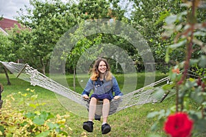 Beautiful girl lying on hammock, smiling resting teenager in spring garden